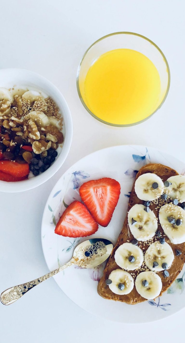 Vollkornbrot mit Banane und Erdbeeren, Schüssel mit Müsli und ein Glas Orangensaft.