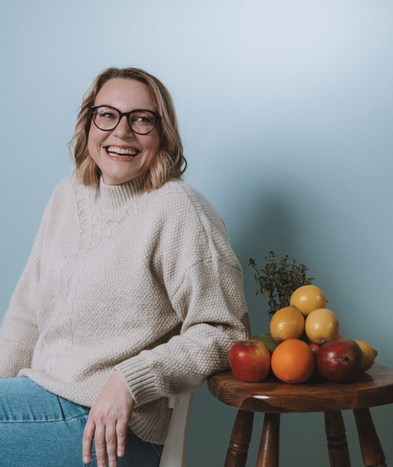 Lächelnde Frau mit Brille und blonden Haaren, trägt ein helles Oberteil.
