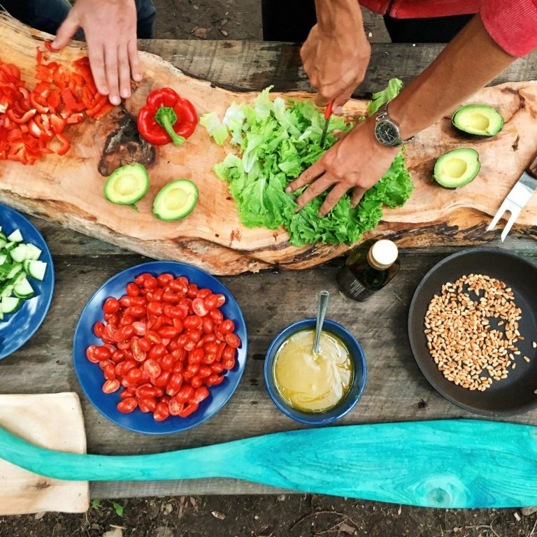 Zubereitung frischer Zutaten wie Tomaten, Paprika und Salat auf einem Holztisch.