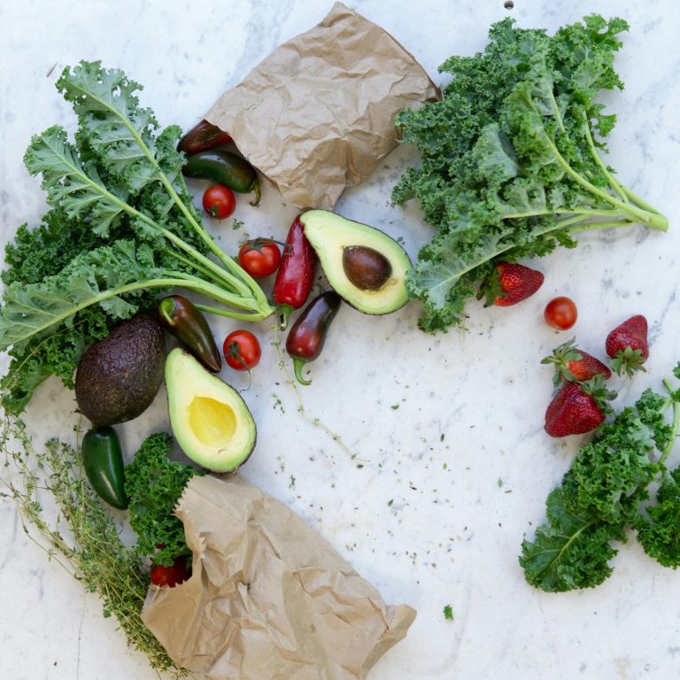 Frisches Gemüse: Grünkohl, Avocado, Cherrytomaten und Jalapeños auf einer Tischoberfläche.