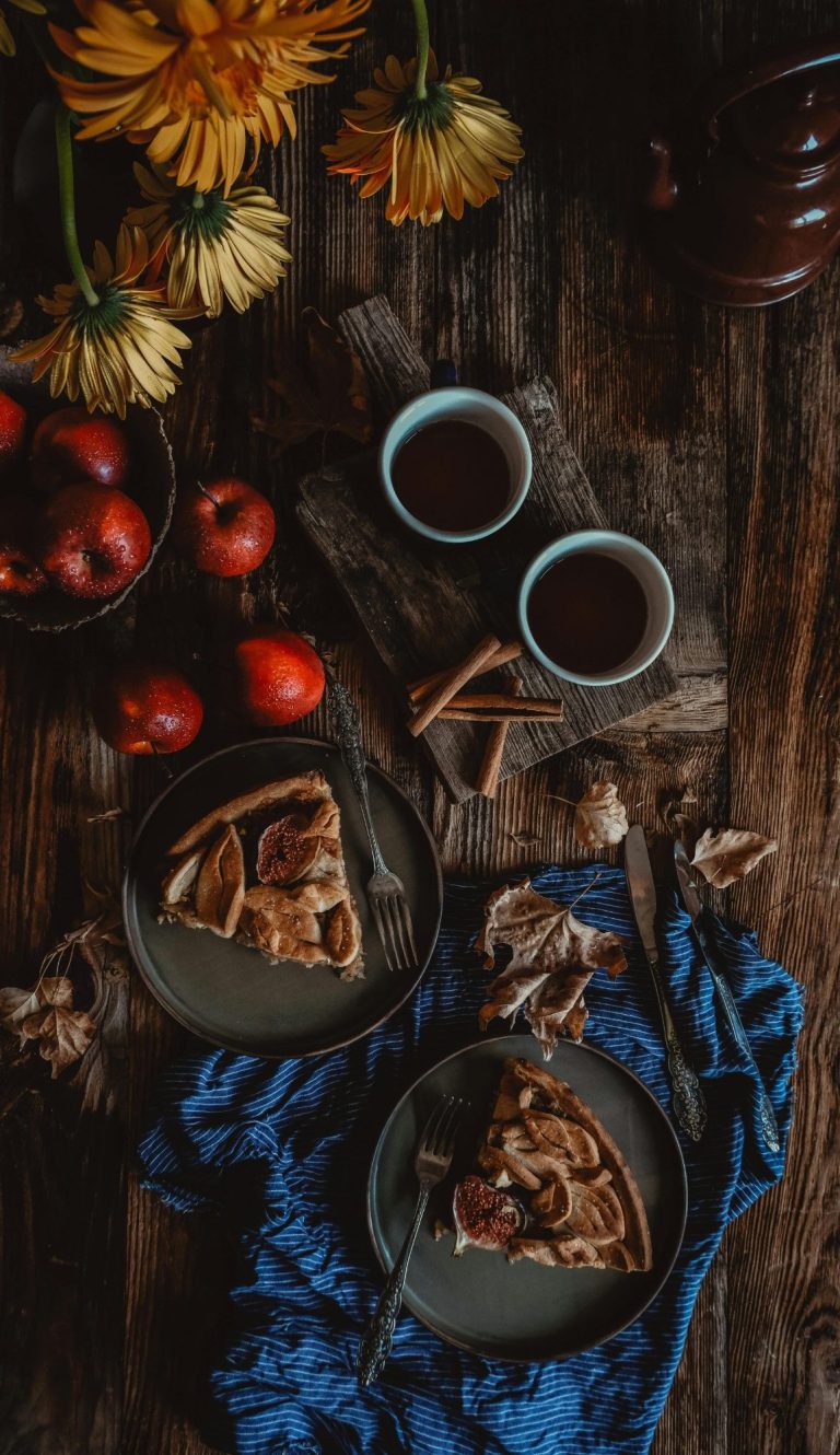 Ein Tisch mit Äpfeln, zwei Tassen Kaffee und zwei Teller mit Kuchenstücken.